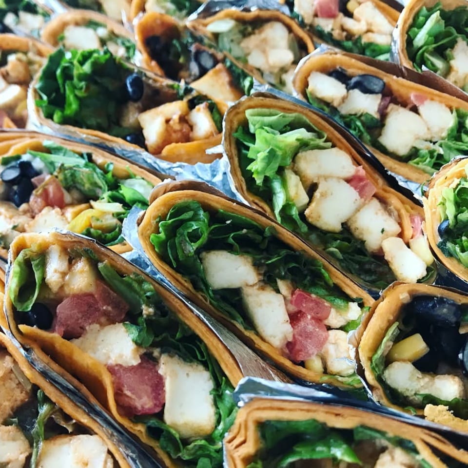 Close-up of multiple vegan tacos filled with lettuce, tofu, black beans, and tomatoes.